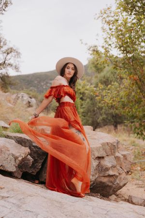 Sheer red dress catches wind dramatically on rocky mountain terrain.