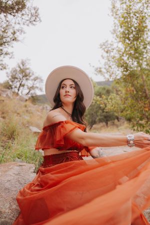 A flowing burnt orange dress catches sunlight against a rocky natural backdrop with mountains in the distance.