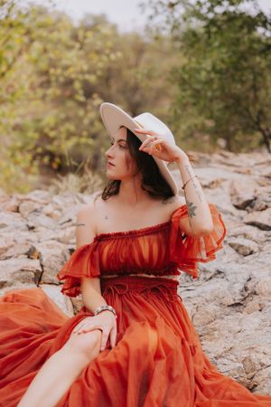 An off-shoulder orange dress and wide-brimmed hat create a romantic outdoor portrait.