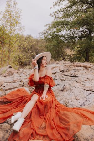 A romantic fashion portrait showcases a flowing orange dress against rocky wilderness.