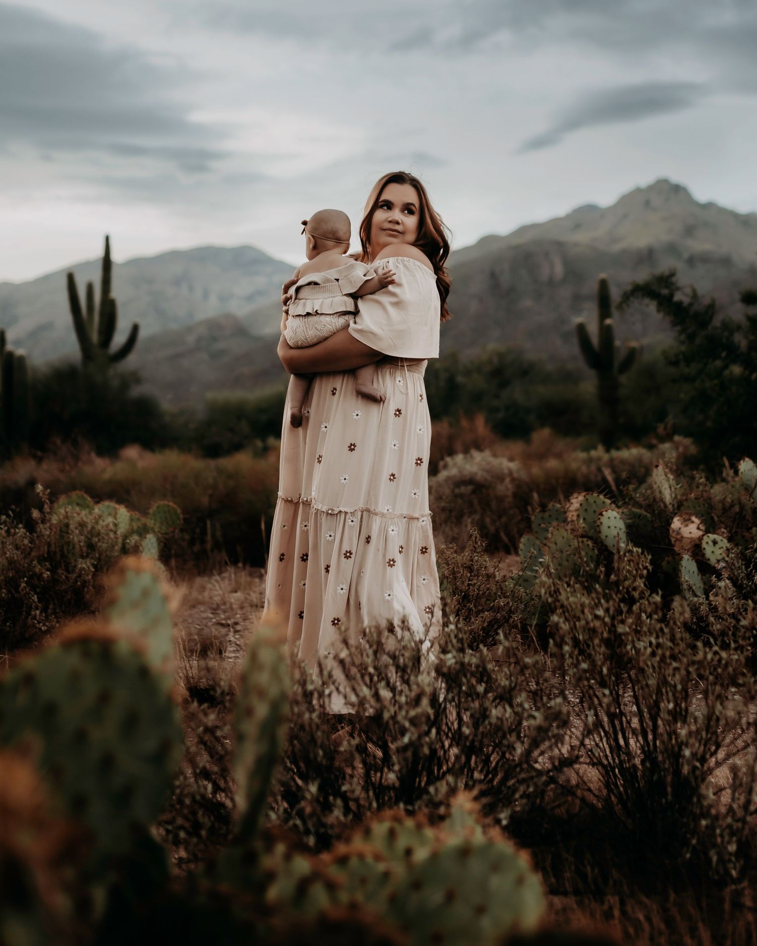 Two people in light colored clothing embracing in a desert landscape with mountains.