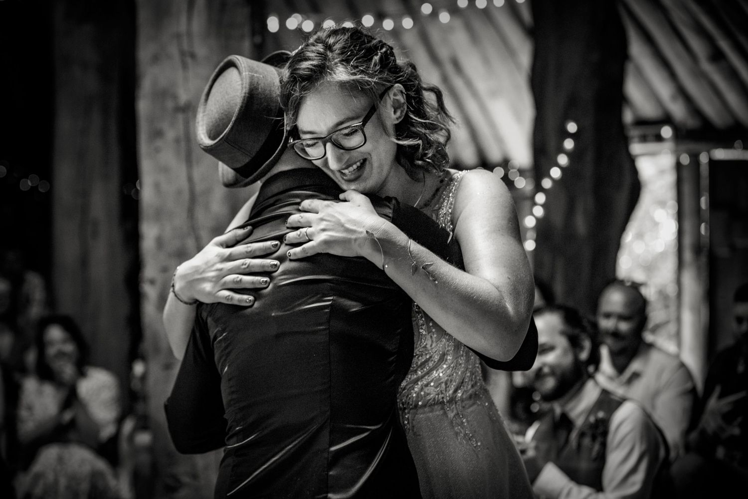 Black and white photo of guests enjoying a wedding reception in a barn setting.