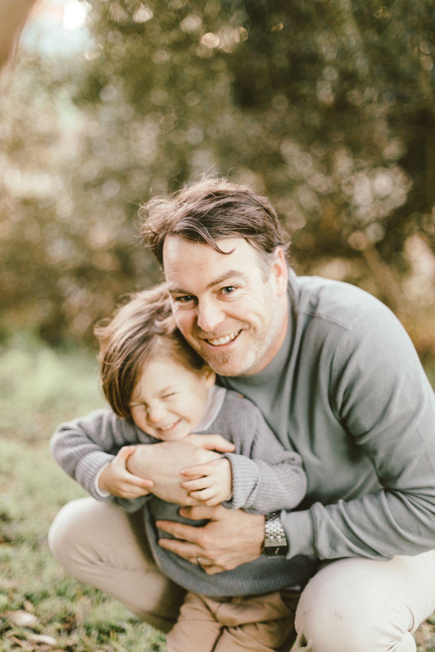 Candid moment of affection between father and child wearing matching grey sweaters outdoors.