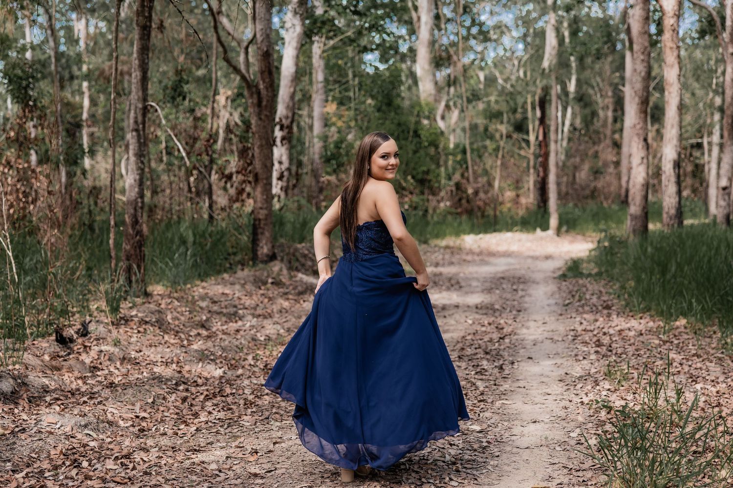 Person in flowing navy blue dress twirling on forest path.