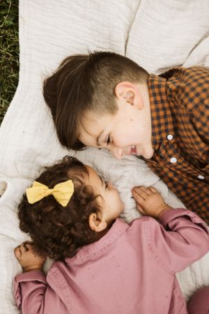 Two children resting close together on a white blanket outdoors.