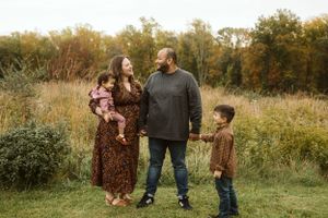 Family of four poses together in a rustic autumn field setting at sunset.