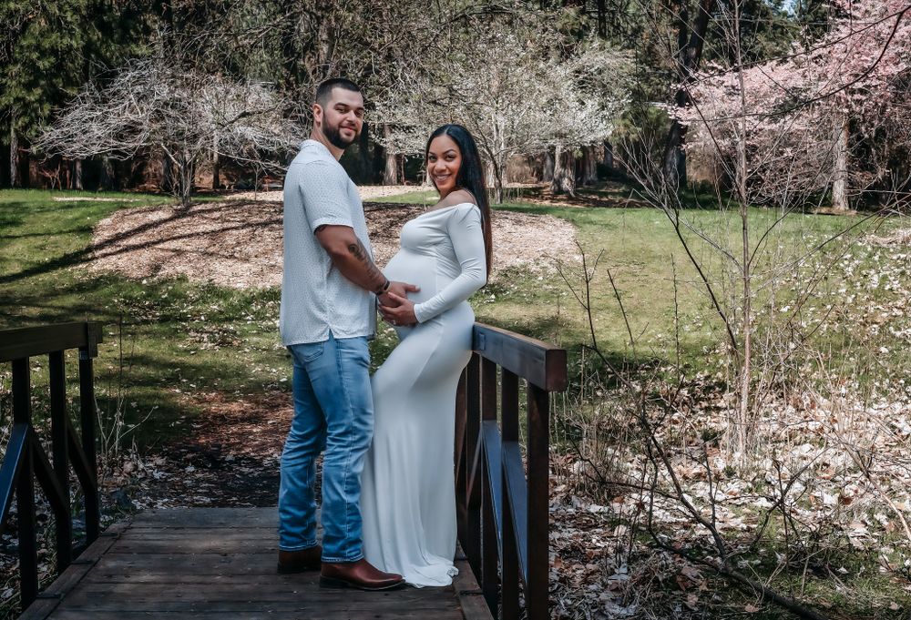 man and pregnant woman embracing in the woods on a wooden bridge