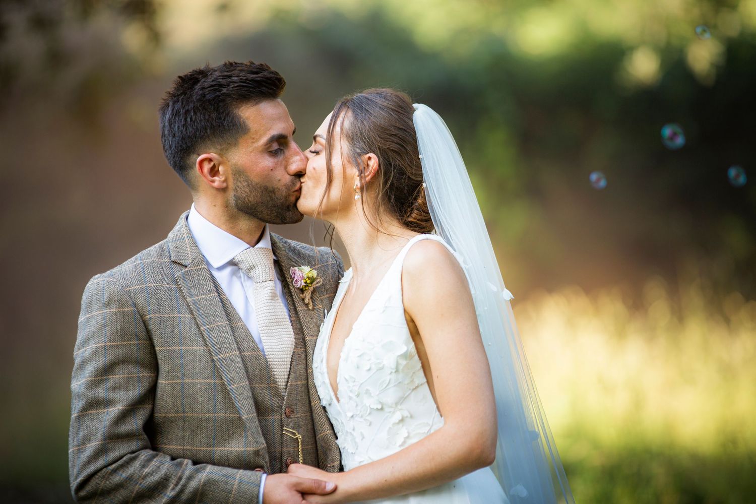 A wedding couple shares intimate moments in a sun-drenched outdoor setting.