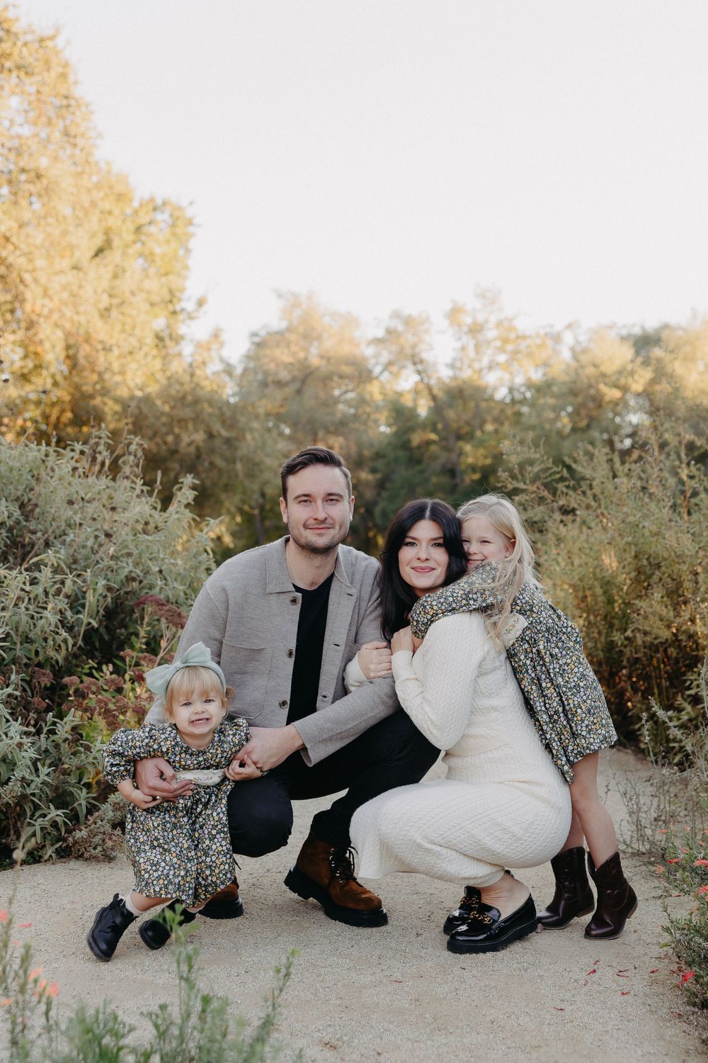 A family kneeling together on a garden path with autumn colors in the background.