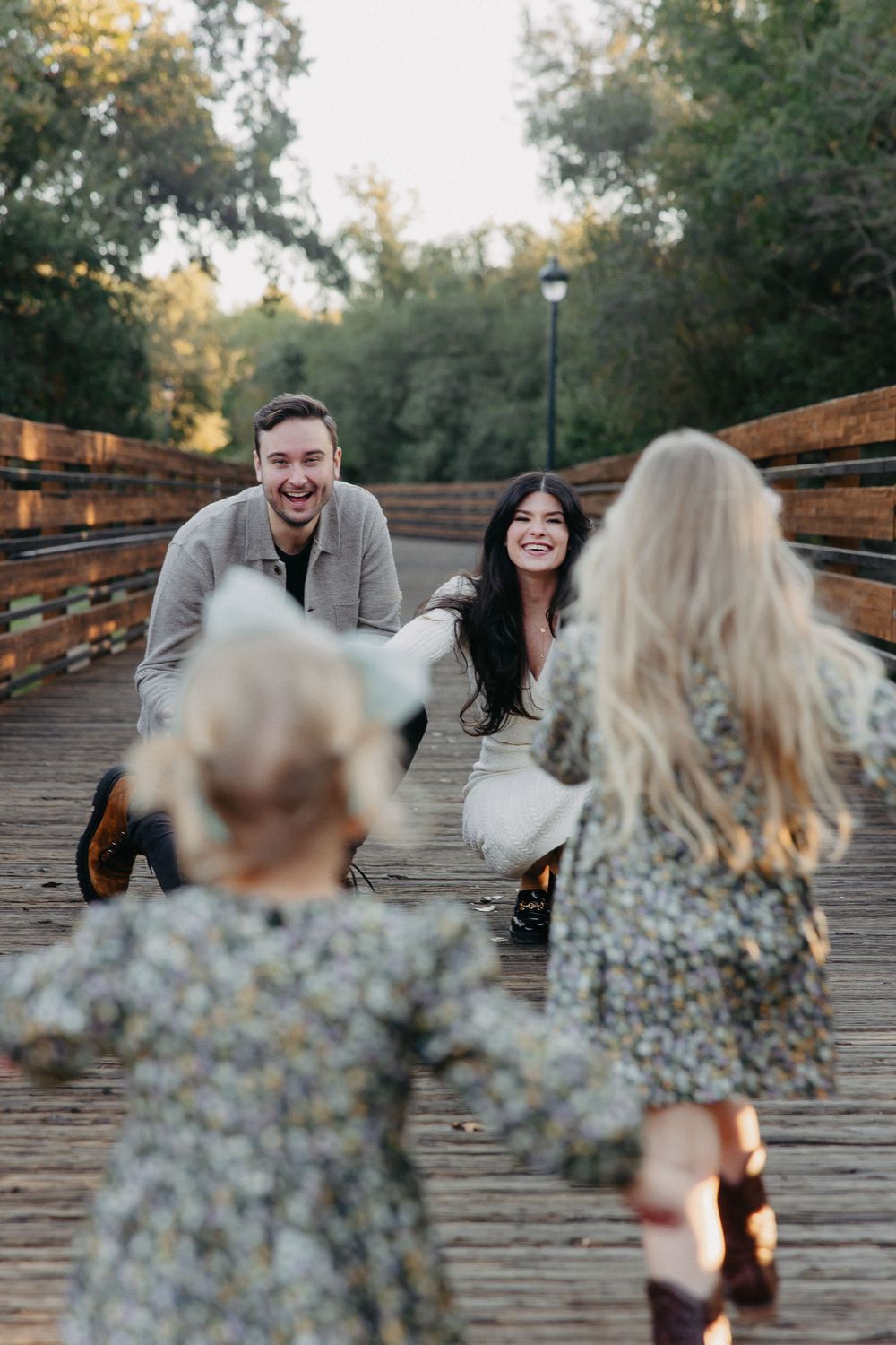 Candid family moment captured on wooden bridge as children run toward parents.