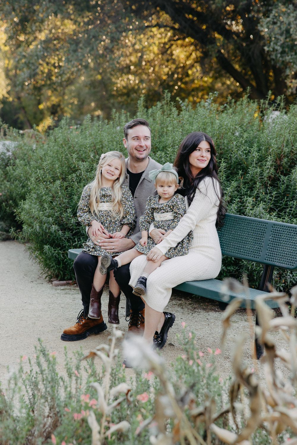 Family in coordinated outfits poses together on a park bench during golden hour.