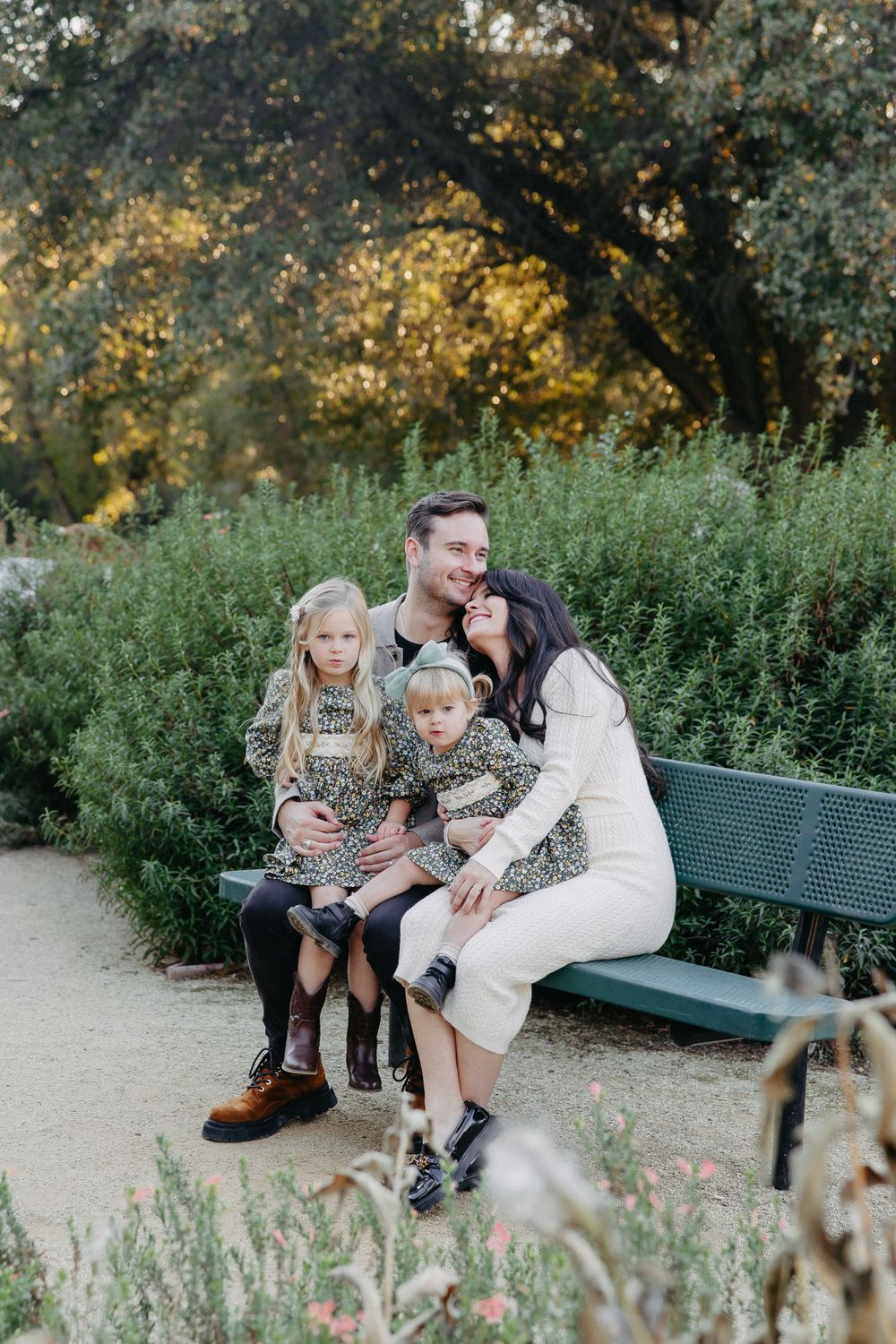 Family sharing a tender moment while sitting on a bench in a garden setting at sunset.