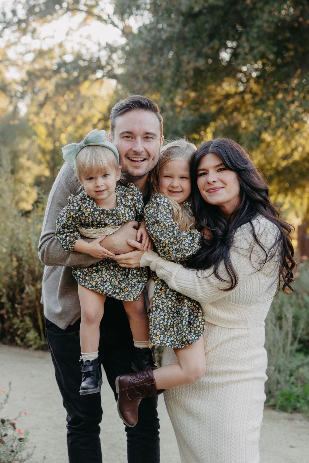A loving family portrait captured outdoors during golden hour with fall foliage in the background.