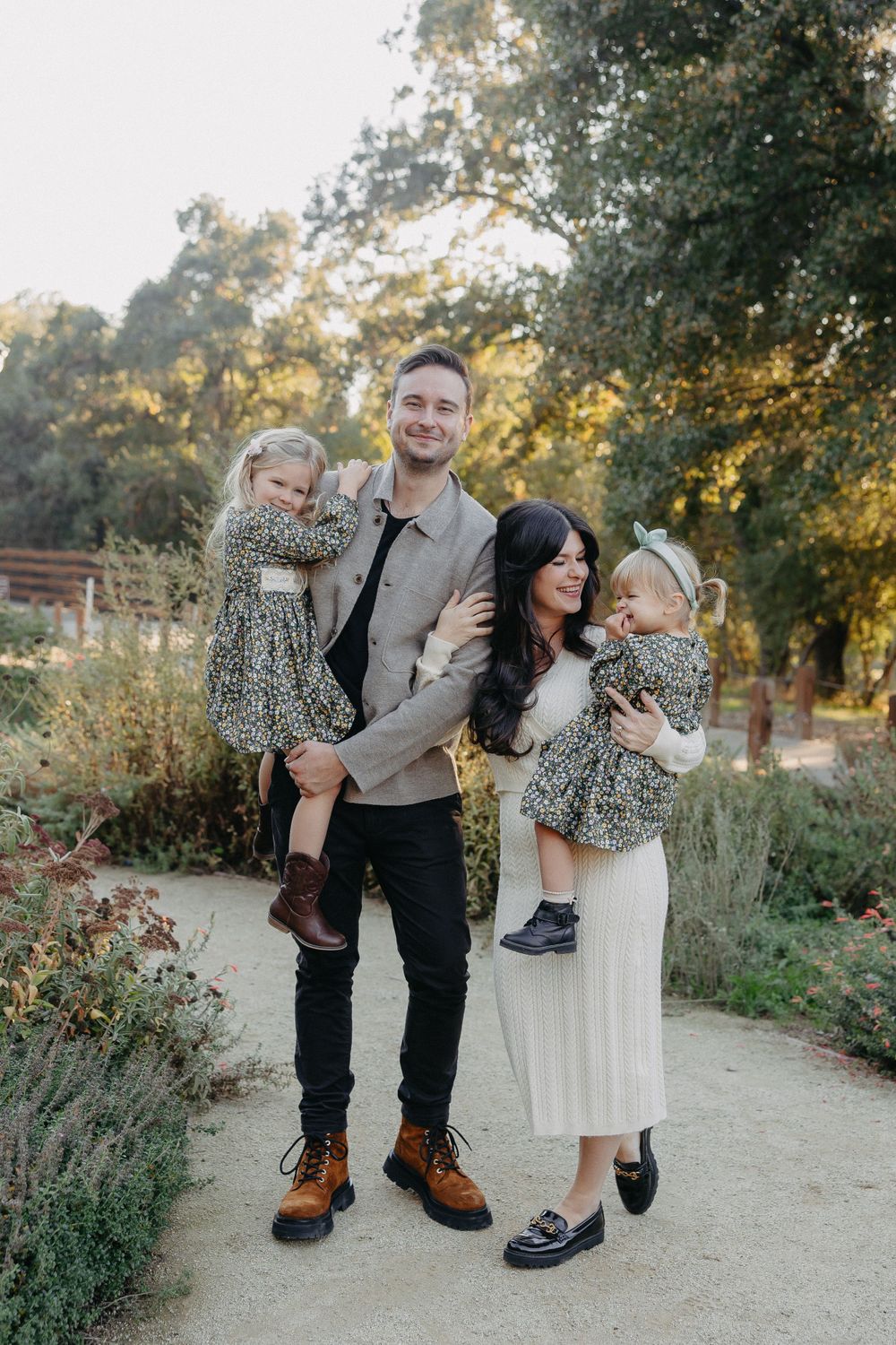 A stylish family wearing coordinated outfits poses on a garden path during sunset.