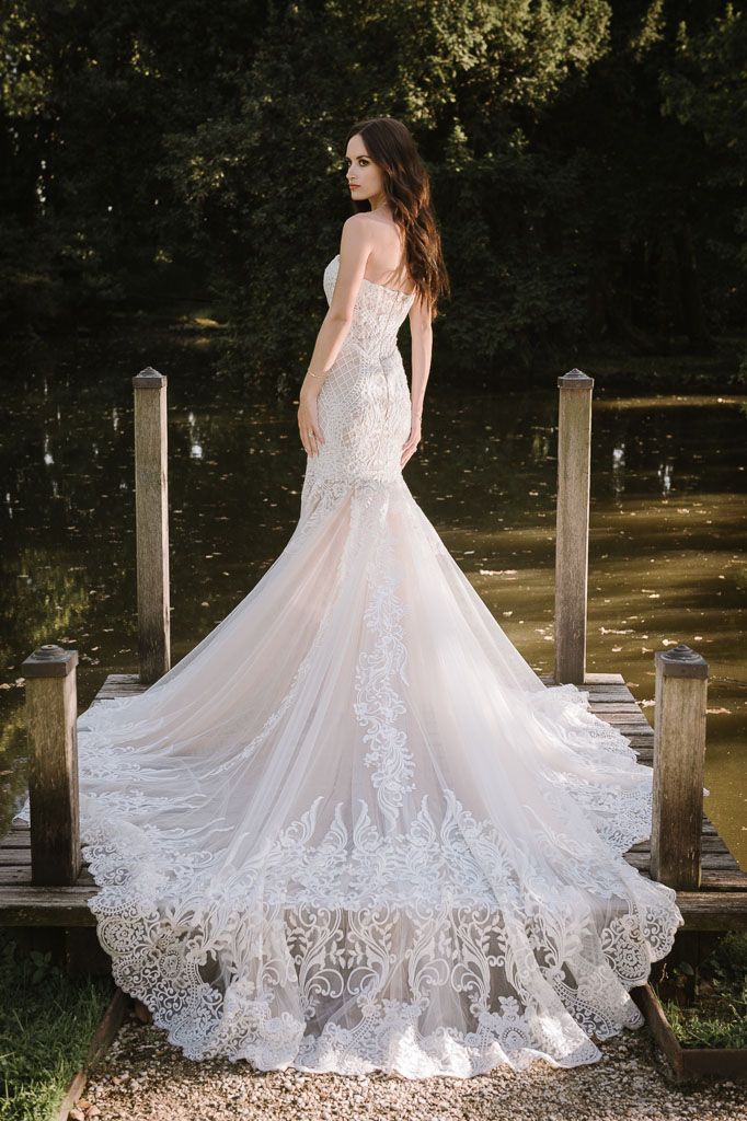 Bride in lace mermaid wedding dress poses on wooden dock with flowing train.