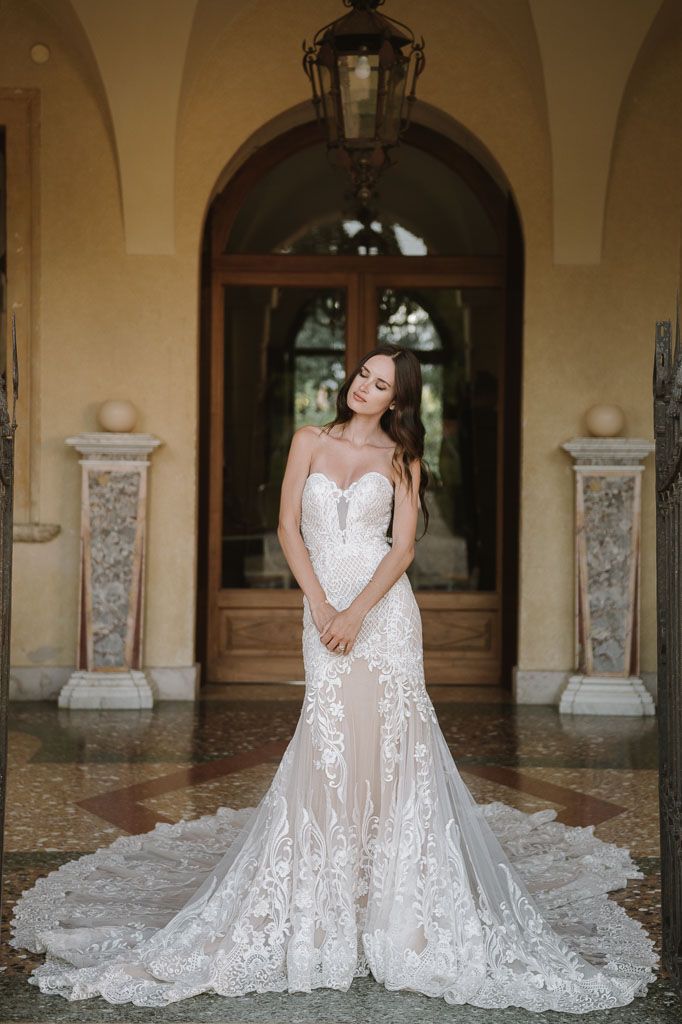 A bride poses in an elegant lace wedding gown with long train under an arched doorway.
