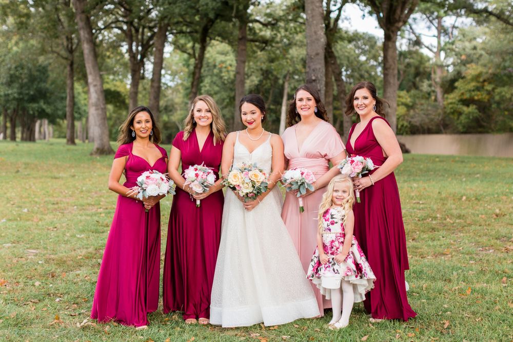 Bridal party in burgundy and pink gowns posing outdoors with bouquets.