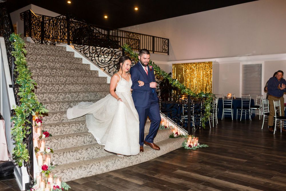 Wedding couple descending elegant staircase with decorative lighting and greenery.