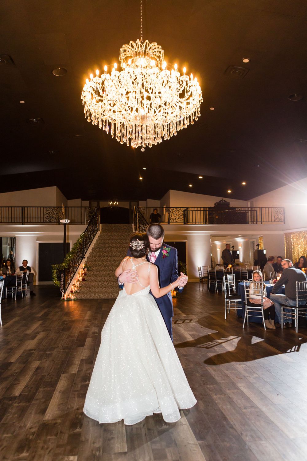 Wedding couple sharing their first dance under a crystal chandelier in an elegant ballroom.