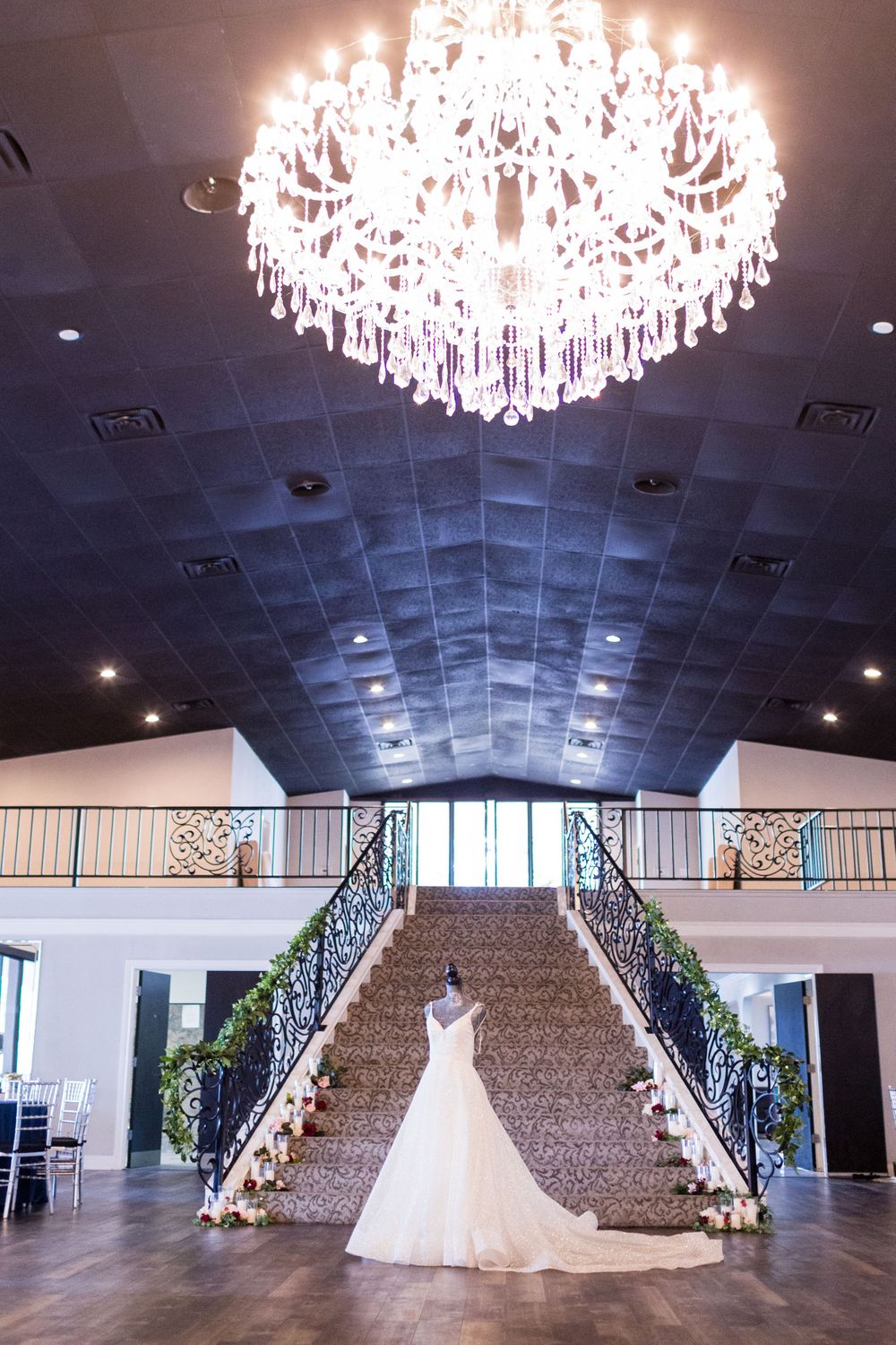 Grand ballroom with crystal chandelier featuring split staircase and white wedding gown display.