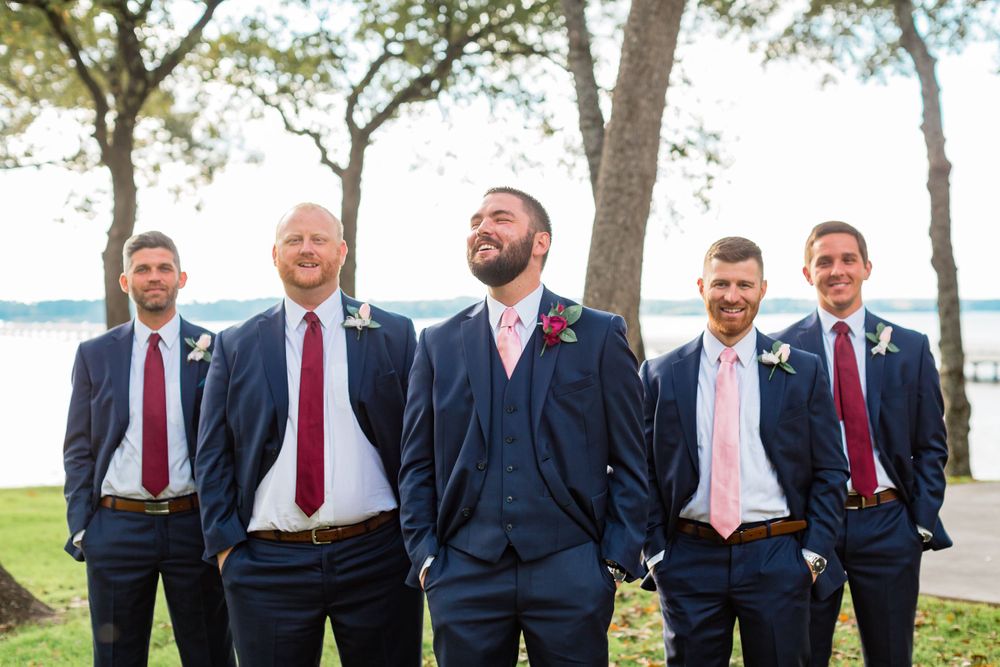 Groomsmen in navy suits and red ties pose by lakefront.