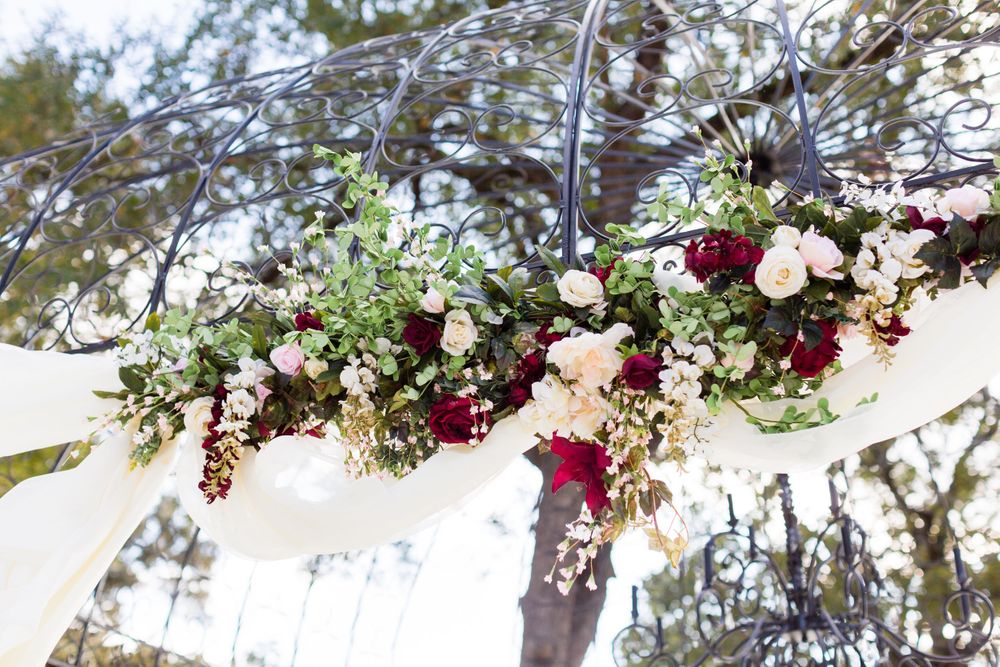 Floral arch decoration with burgundy and white roses against draped white fabric.