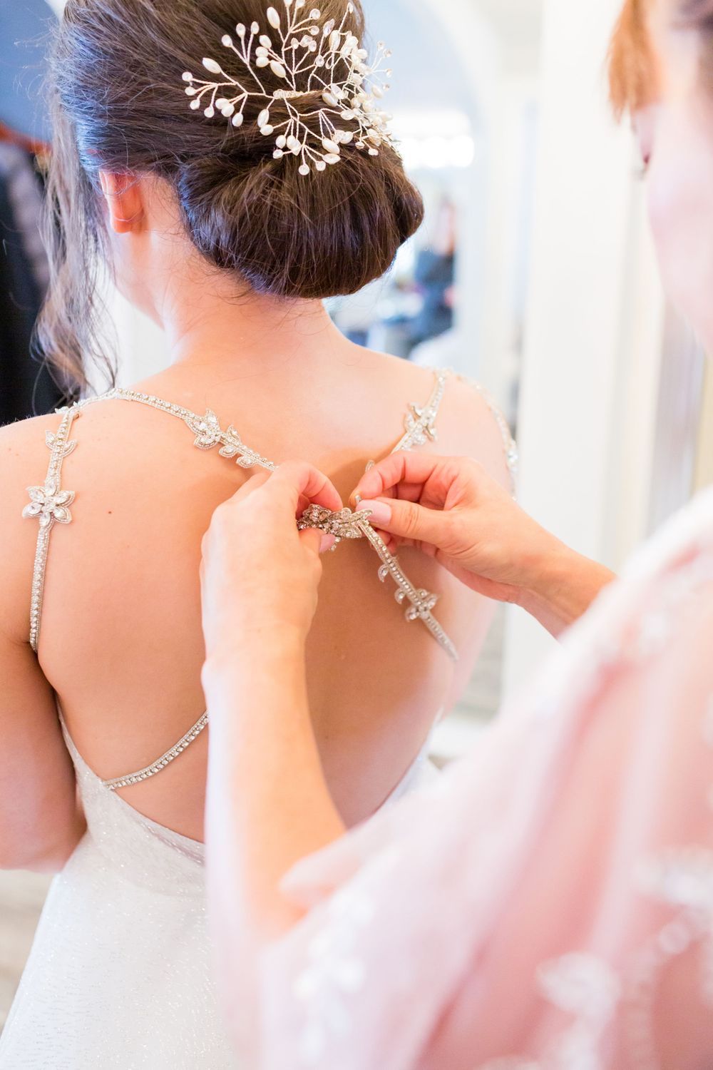 Detailed shot of sparkly bridal hair accessory and back necklace being fastened.