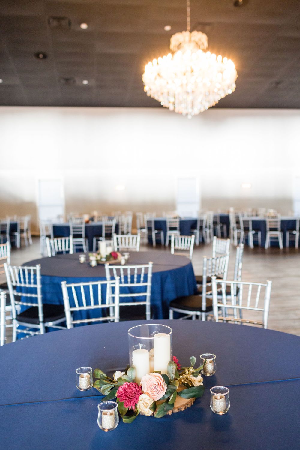 Elegant wedding reception setup with navy tablecloths and crystal chandelier in a spacious ballroom.