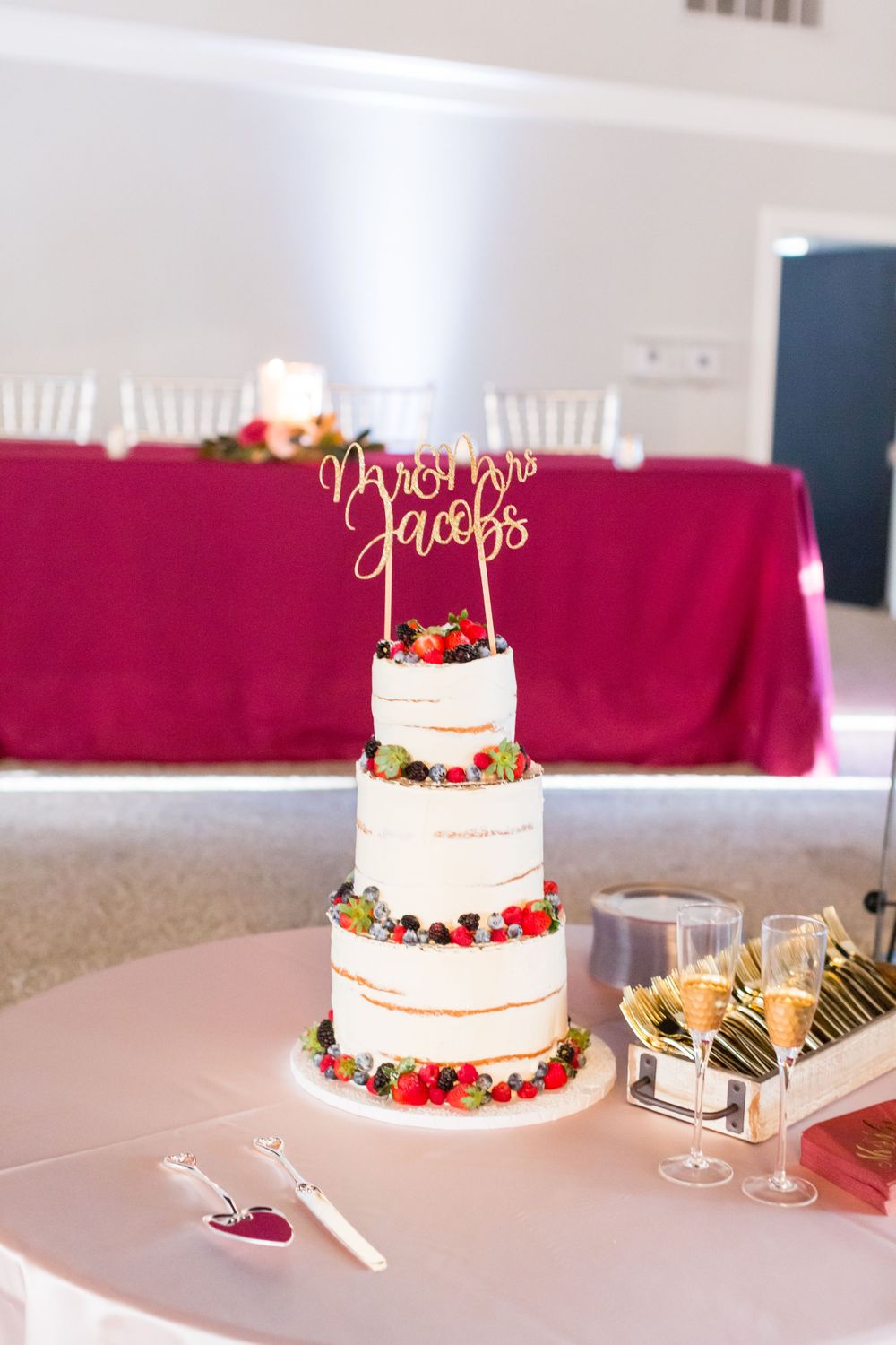 Three-tiered white wedding cake decorated with fresh berries and gold cake topper.