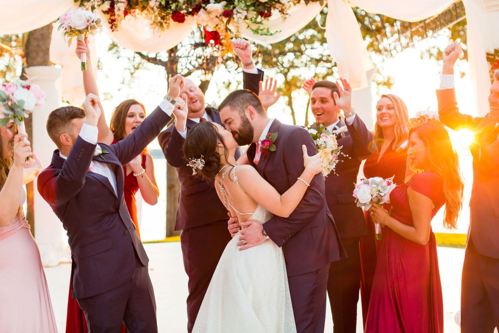 Wedding party celebrating at sunset under string lights and floral decorations.