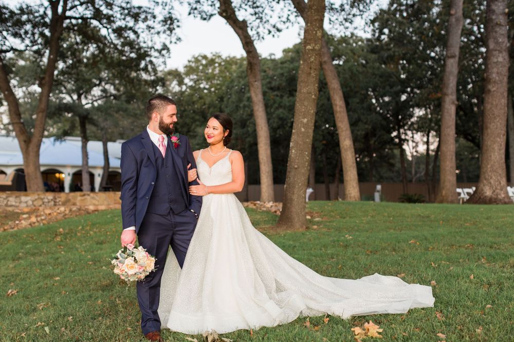 Newlyweds pose together on grassy lawn with lake view and flowing wedding dress.