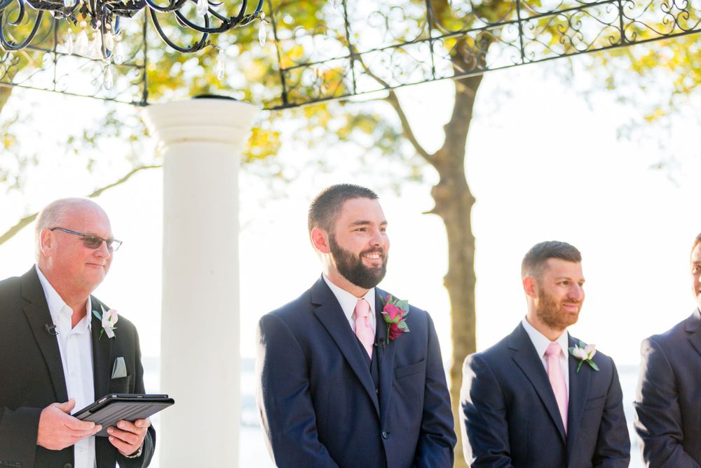 Wedding ceremony under white columns with groomsmen in navy suits.