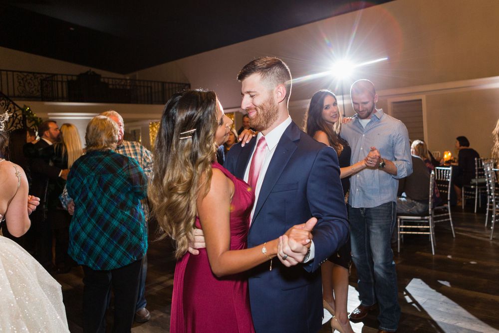 Couples dance together during a wedding reception in an indoor venue with silver chiavari chairs.