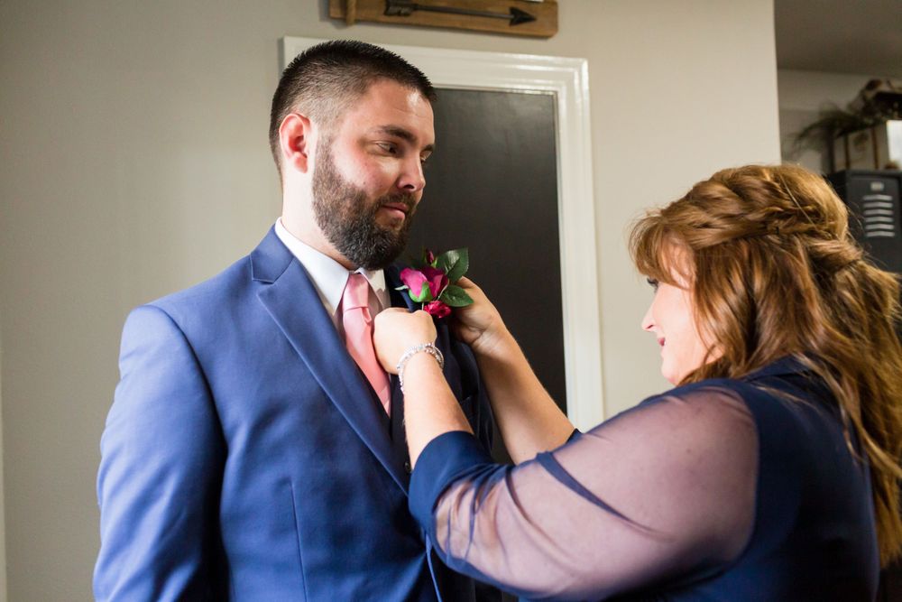Final adjustments being made to a pink boutonniere on a blue suit jacket.