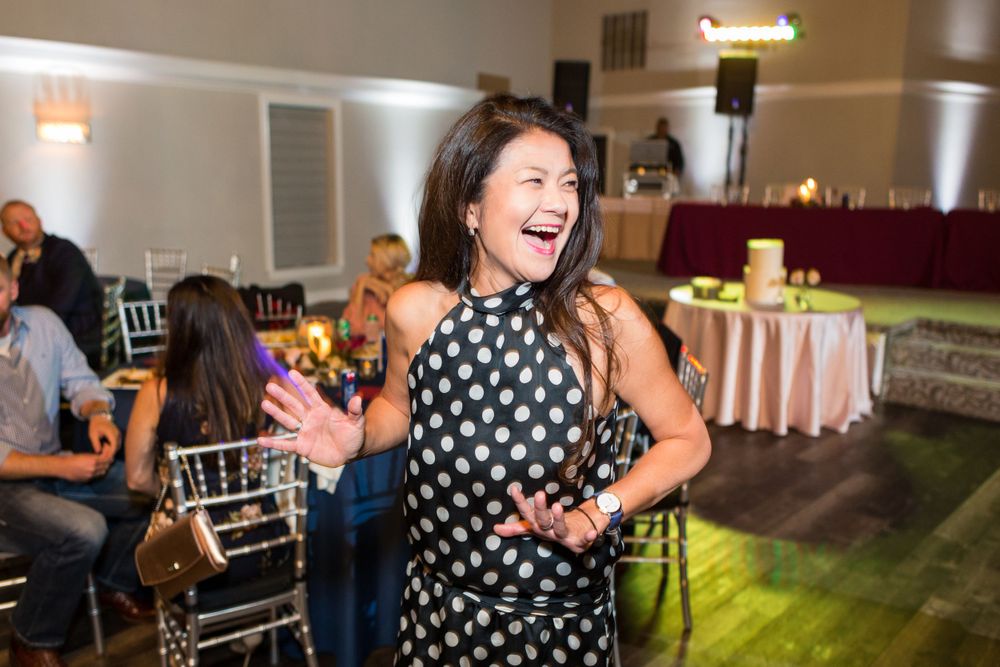A guest in a polka dot dress dances enthusiastically at a wedding reception.