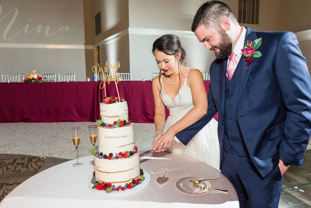 A couple cuts their three-tiered white wedding cake decorated with fresh flowers.