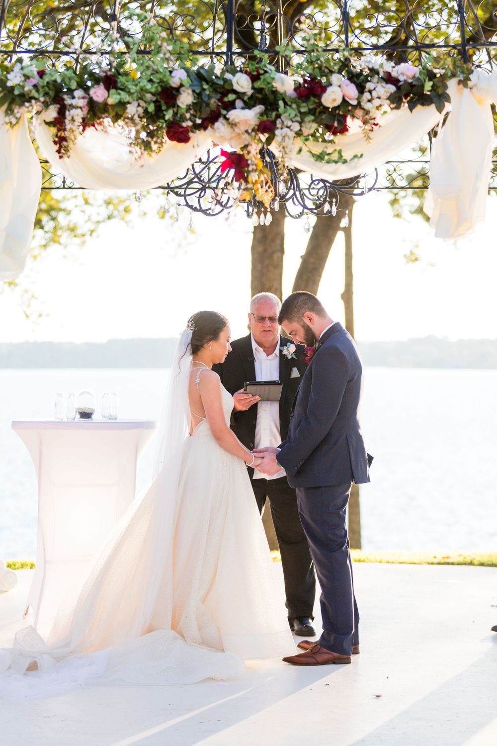 Intimate waterfront wedding ceremony under an elegant floral-decorated arch.