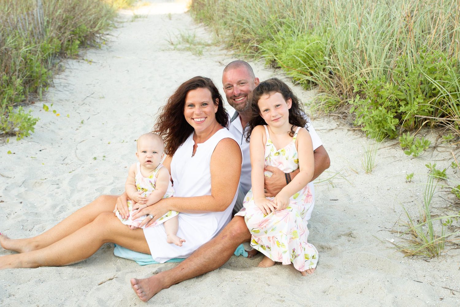 A family sits together on a sandy beach path surrounded by beach grass.