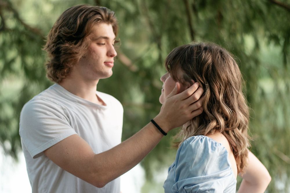 A tender moment between a couple against a backdrop of green trees.