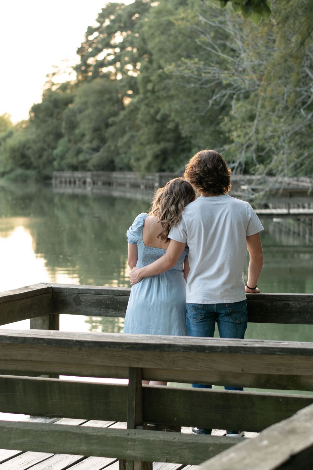 A couple embracing while looking out over a tranquil lake from a wooden deck.