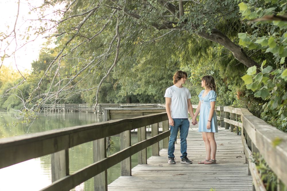 A couple walking together on a wooden boardwalk overlooking a peaceful lake at sunset.