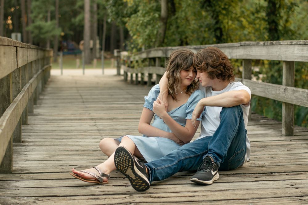 A couple sitting close together on a wooden boardwalk surrounded by nature.