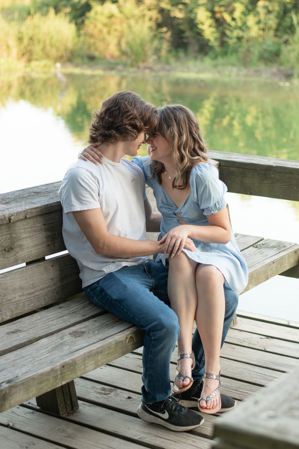A romantic couple sharing a tender moment while sitting on a wooden bench by the water.