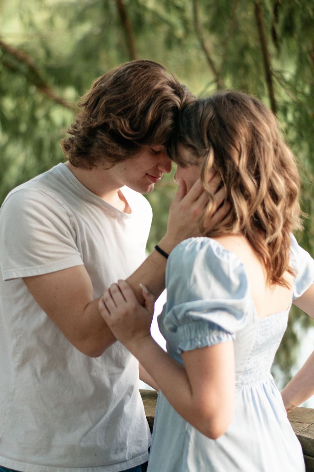A romantic couple sharing an intimate moment outdoors under green foliage.