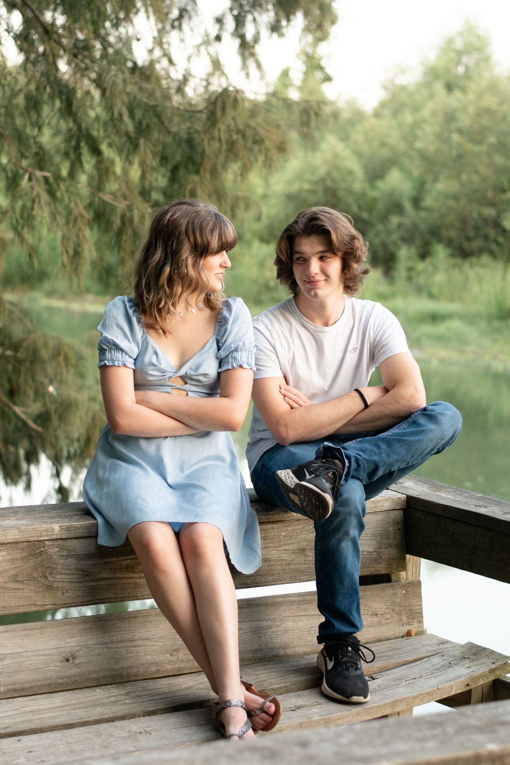 A couple in casual attire sitting on a wooden deck overlooking a lake.