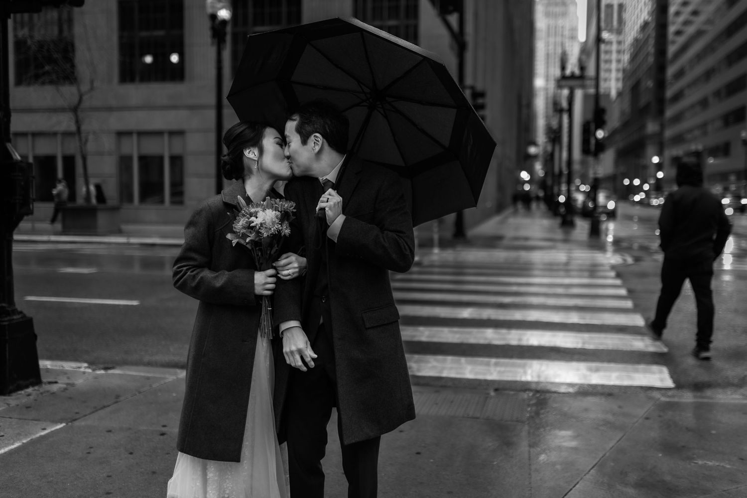 A couple shares an intimate moment under a black umbrella on a rainy city street.