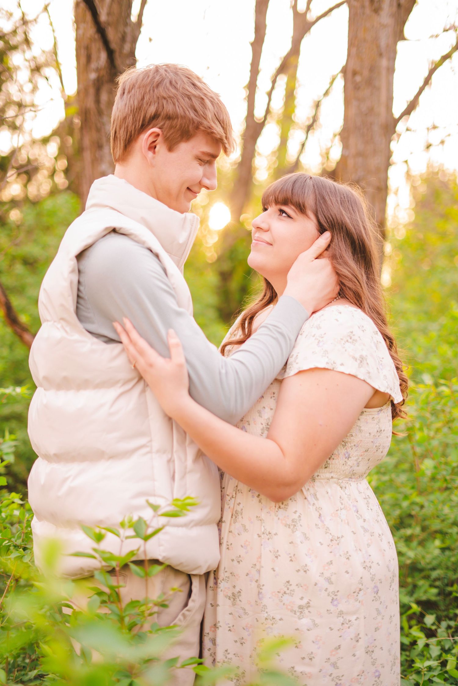 Young couple gazing at each other tenderly in sun-dappled green forest during golden hour.