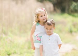 Two children stand together in a field of tall grass on a sunny day in Beaufort, SC for family photography session.
