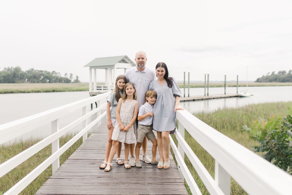Family of five poses together for a photograph on a white wooden dock overlooking marsh landscape in Habersham, SC.
