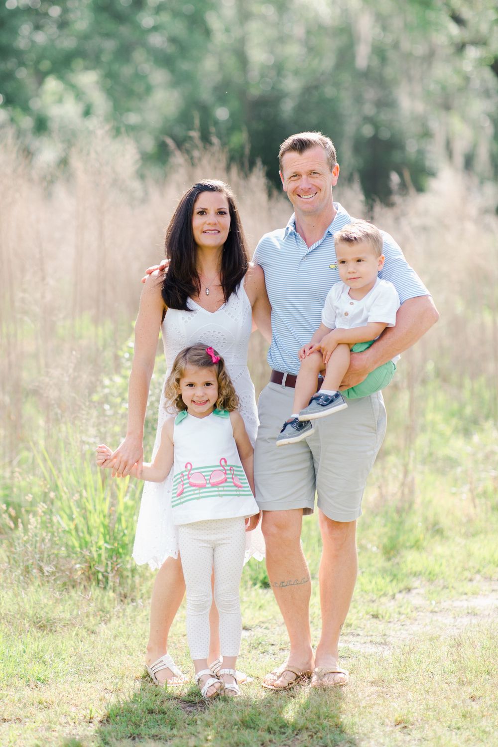 Family photography of four posing together in a sunlit field with tall grass in Beaufort park by local photographer.